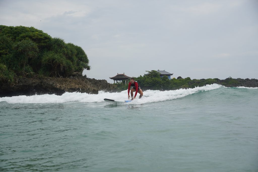 A man tries to stand on his surfboard while riding gentle waves at the Nusa Dua - Blackstone surf spot with Surf Journey Bali.