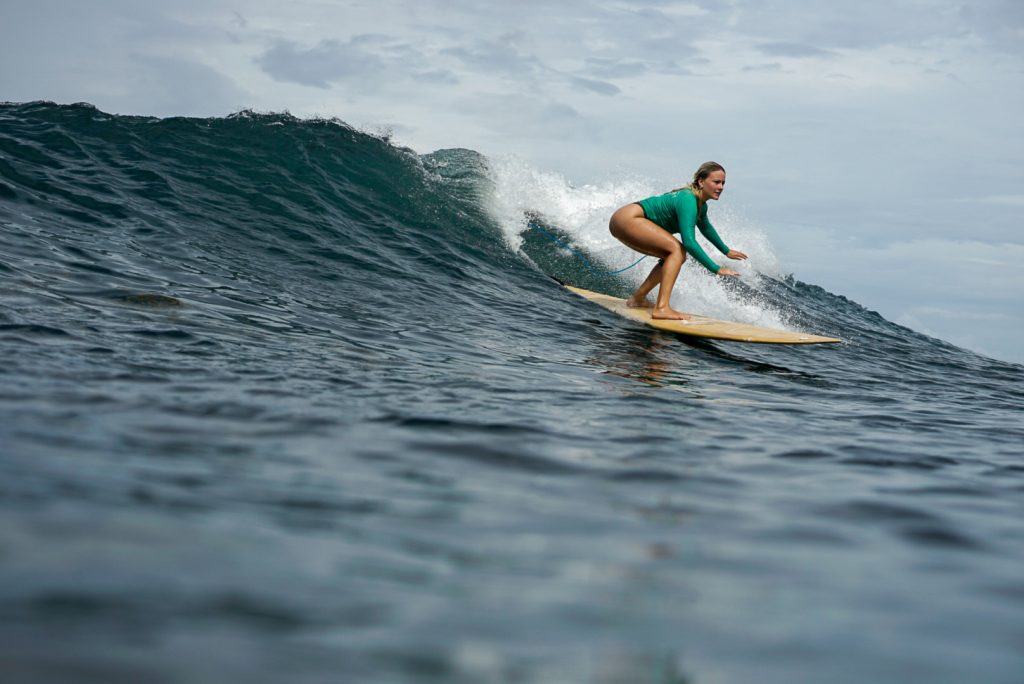 A woman stands completely balanced on large, steady waves on the west coast of Bali during the dry season with Surf Journey Bali