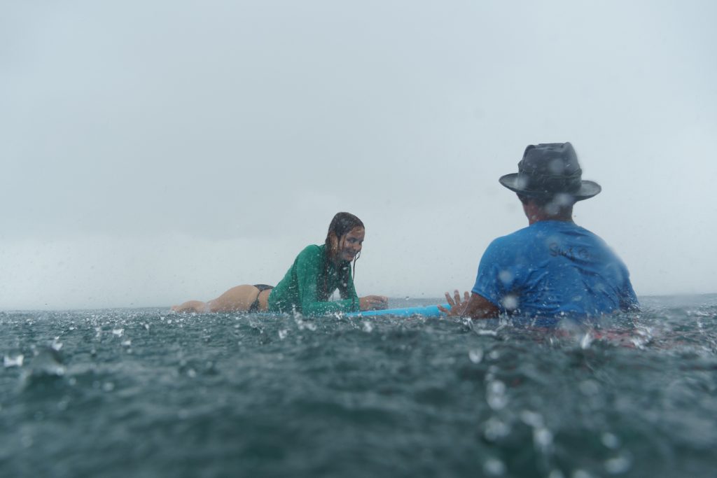 A woman has fun surfing during the wet season with our coach at Surf Journey Bali.